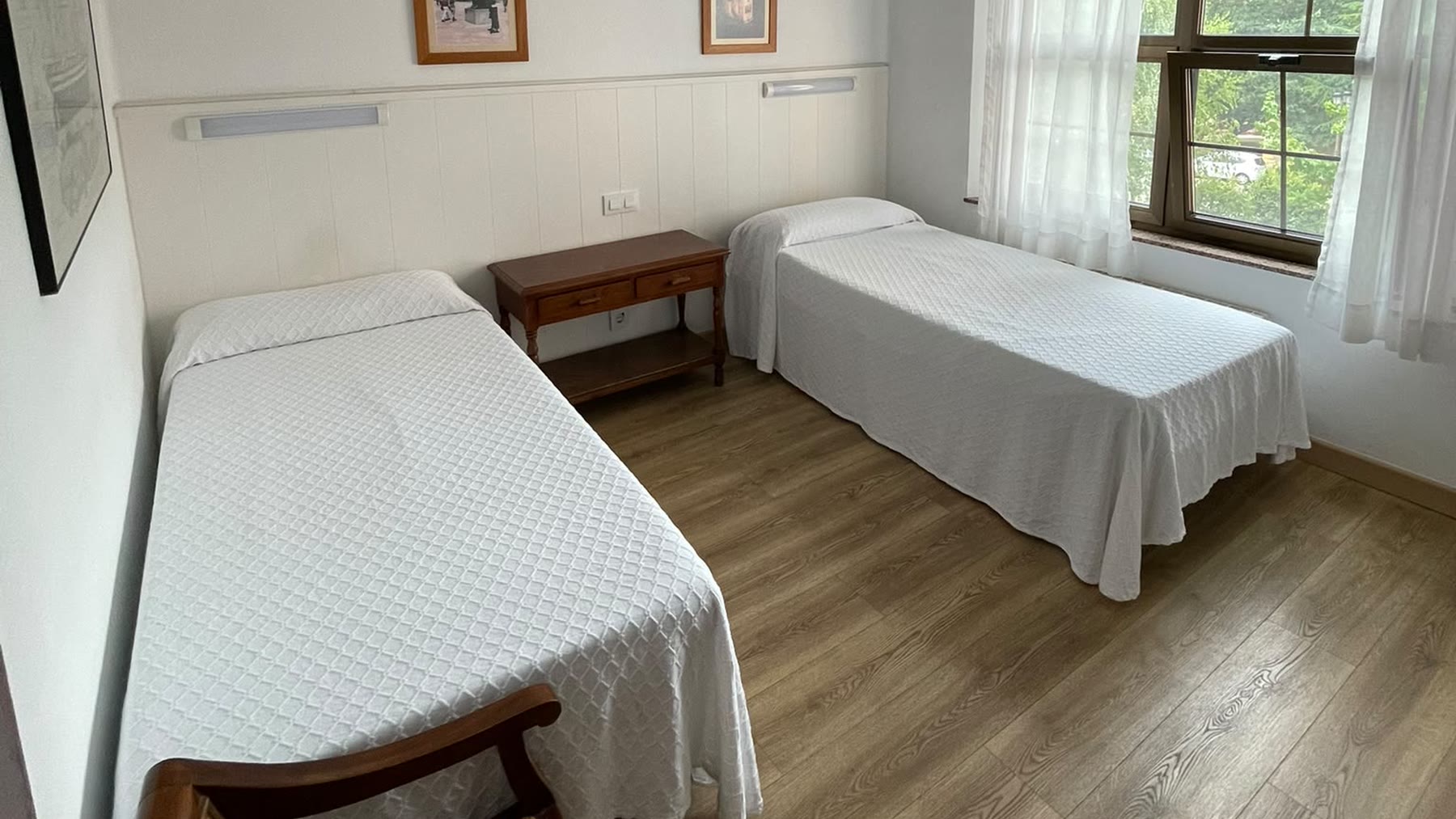 Habitación doble con dos camas, ventana a los árboles del jardín y suelo de madera