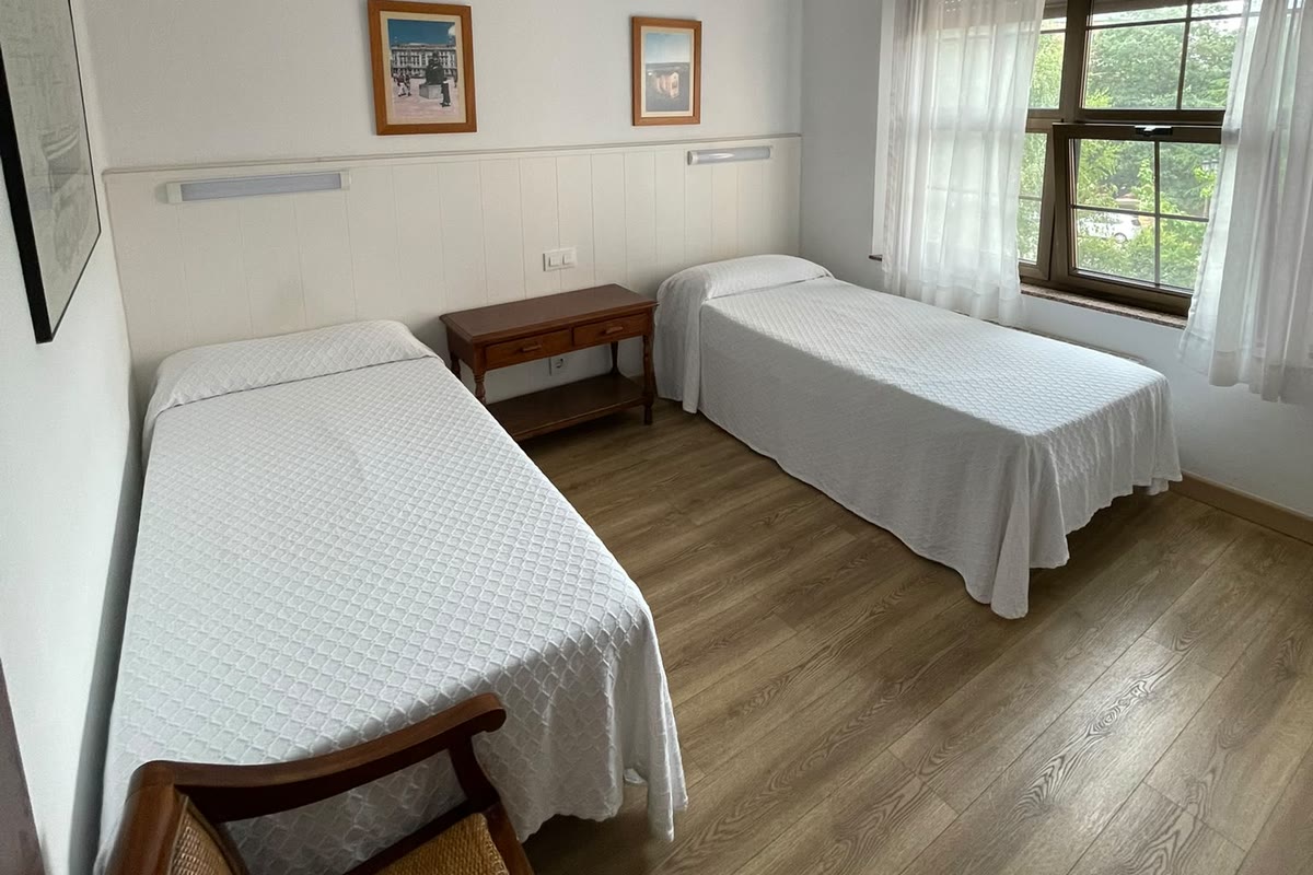 Habitación doble con dos camas, mesilla de madera y ventana a los árboles