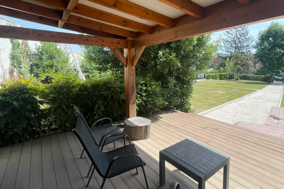 Porche de madera con butacas, abierto a la pradera del jardín
